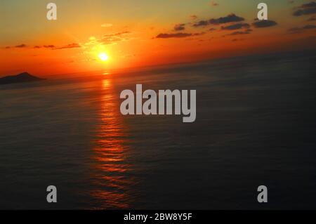 Der orangefarbene Himmel spiegelt sich über das ruhige Wasser der Maunalua Bay mit Diamond Head-Silhouette am Himmel. Schiff fährt nach Oahu, Hawaii Hafen. Bild ist hig Stockfoto