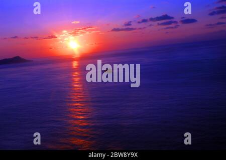 Die hohe und schräg anfallende Ansicht des Sonnenuntergangs über Diamond Head zeigt Sonnenstrahlen, die sich auf dem ruhigen Wasser der Bucht vor Oahu, Hawaii, spiegeln. Schiff langsam geht zu por Stockfoto