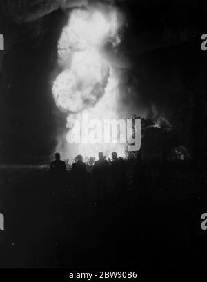 Die Silhouetten der Männer sind gegen die Flammen und den Rauch des Feuers auf der Reifenhalde in Ruxley, Kent, zu sehen. Juni 1937 Stockfoto