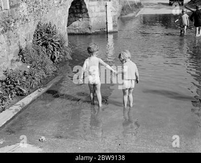 Kleine Kinder paddeln in der ford an der Buckelbrücke von Eynsford über den Fluss Darent in Kent. 1939 . Stockfoto