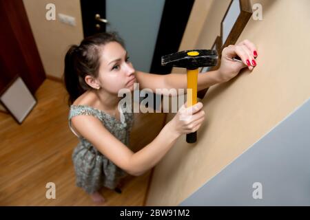 Junge Frau, Hammer, Nagel und Wand. Männliche Arbeit von weiblichen Händen durchgeführt Stockfoto