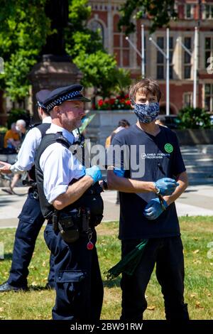 30. Mai 2020 London, UK - Extinction Rebellion inszeniert schweigenden sozial distanzierten Klimawandel-Protest in Westminster, Demonstranten, die von der Polizei wegen Verletzung der Coronavirus-Vorschriften bestraft und weggebracht werden, Mann in Gesicht Maske in Handschellen, verhaftet und von Polizisten festgehalten Stockfoto