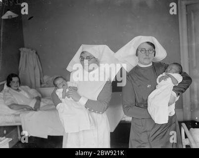 Unter den wachsamen Augen ihrer Mütter halten zwei Krankenschwestern Leap Year Babys in den Armen im Erith Mutterschaftskrankenhaus. 1936 Stockfoto