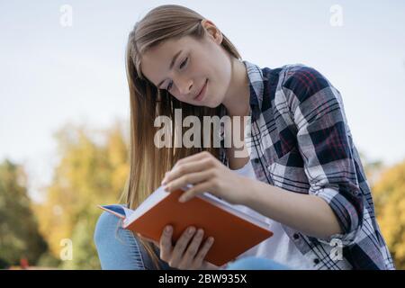 Schöne Frau, die im Park Buch liest. Nahaufnahme Porträt des lächelnden Studenten Sprache lernen, Prüfungsvorbereitung, sitzen auf Bank. Bildungskonzept Stockfoto