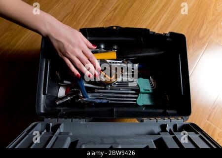 Mädchen mit roter Maniküre greift nach den Werkzeugen in der Werkzeugkiste. Frauen und Männer arbeiten Stockfoto