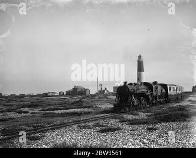 Die Romney, Hythe & Dymchurch Light Railway endet am Dungeness Beach. Dieser Motor verlässt den Bahnhof, der sich neben dem alten Leuchtturm befindet. Die Romney, Hythe & Dymchurch Railway ist eine 15 in/381 mm Spur leichte Eisenbahn in Kent, England. Die 131/2-Meile (22 km) Linie verläuft vom Cinque Port of Hythe über Dymchurch , St. Mary's Bay , New Romney und Romney Sands nach Dungeness . 1936 Stockfoto