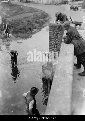 Arbeiter waten durch das Wasser überqueren an der Eynsford Brücke über den Fluss Darent in Kent. 1936 . Stockfoto