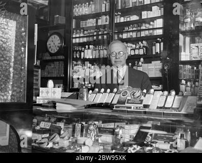 Ladenbesitzer von Banditen in London gefesselt. Herr George Rackham, ein Assistent in einem Chemiker-Shop in Charing Cross Road, London, wurde von Banditen, die ihn mit Stäuben und Schnur und beraubt ihn, nahm Geld in der Kasse in der Shop, und floh mit dem Auto. Herr George Rackham hinter dem Ladentisch, in dem er von Banditen angegriffen wurde. Mai 1932 Stockfoto