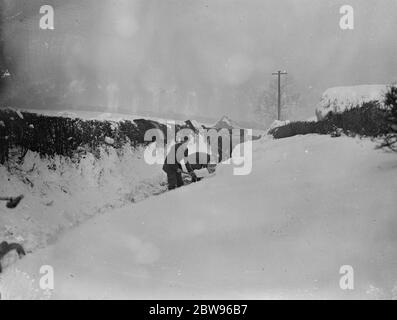 Drifts von Schnee vier Meter tief Block Surrey Straßen zum Verkehr. Drifts von Schnee mehr als vier Fuß in der Tiefe haben Straßen in Surrey und Kent blockiert und machte sie unpassierbar für den Verkehr, Armeen von Männern sind bei der Arbeit Clearing der Straßen. Schneeräumung auf einer Straße in Tatsfield, Surrey, wo Drifts sind mehr als vier Meter in der Tiefe. 13 Februar 1932 Stockfoto