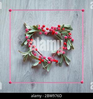 Weihnachtskranz in Form von Mistel mit roten Beeren hängen an rustikalen Holztür, traditionelle Weihnachtsschmuck. Minimalistisch trendy Weihnachtsdekor, rosa Fr. Stockfoto