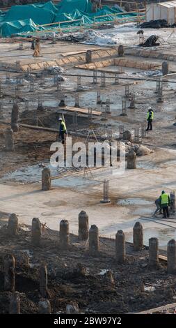 Draufsicht der Baustelle mit Stahlbetonpfählen und Arbeitern, vertikal. Arbeit an der Vorbereitung der Fundamente des Gebäudes. Stockfoto