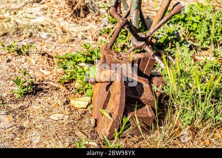 Alte, rostige Metallschrauber, Radstrebe und Achse stehen in rauem Gras. Verworfene Werkstattwerkzeuge sind dem Verfall überlassen. Rekord Nr. 3 Industrieschraubenstock aus Gusseisen. Alt Stockfoto