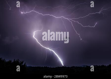 Zwei dramatische Blitze, die über dem Boden abfallen und ein lila Himmel nachts in Rumänien über dem ländlichen Raum Stockfoto