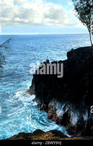 Einheimische Fischer fischen am Rande einer großen Klippe im McKinzie State Park auf der Windseite der Big Island von Hawaii. Gegen die fo Stockfoto