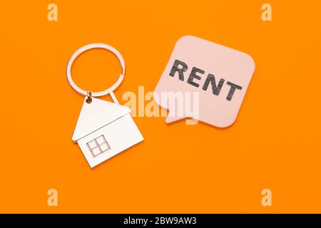 Mietkonzept. Metall Schlüsselanhänger in Form eines Hauses und ein Aufkleber mit der Aufschrift - Miete auf einem orangefarbenen Hintergrund. Stockfoto