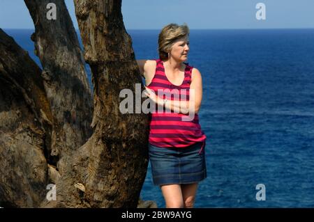 Tourist lehnt sich an einen rustikalen Baumstamm und genießt die Sonne und den Wind weht, wie sie den Blick aus dem nördlichen Punkt der Big Island von H genießt Stockfoto