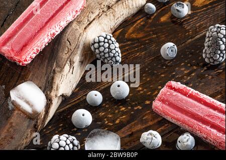 Gefrorene Beeren, Eislollies und Eiswürfel über einem Holzbrett Stockfoto