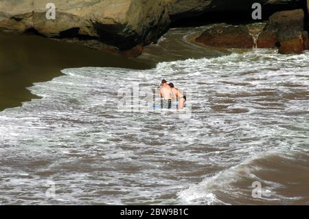 Dreiköpfige Familie spielt in den Wellen am Green Sand Beach auf der Big Island von Hawaii. Mama und Papa lehren ihr Kleinkind, wie man ein Boogie Board benutzt. Stockfoto