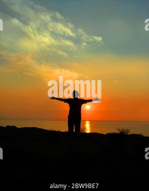 Besucher steht mit breiten Armen und verabschiedet sich von der Big Island von Hawaii. Die Sonne geht unter und endet den Tag, während ihre Reise ebenfalls endet. Stockfoto