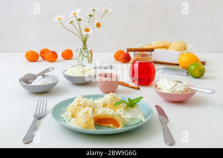 Mit Aprikosen gefüllte Fruchtknödel, bestreut mit Quark und Zucker, übergossen mit geschmolzener Butter, mit Creme fraiche mit geriebener Limettenschale an Stockfoto