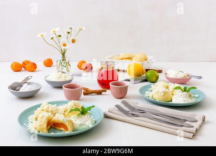 Mit Aprikosen gefüllte Fruchtknödel, bestreut mit Quark und Zucker, übergossen mit geschmolzener Butter, mit Creme fraiche mit geriebener Limettenschale an Stockfoto