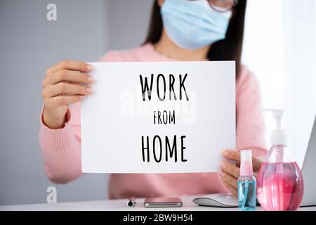 Geschäftsfrau Hand hält weißes Papier mit Arbeit von zu Hause Text. Laptop-Maus-Smartphone, Desinfektionsmittel Gel, medizinische Gesichtsmaske und Alkohol Spray für Pre Stockfoto