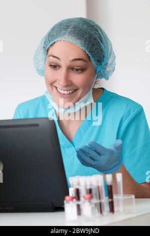 Frau in schützenden labÂ workwearÂ sitzt vor dem Laptop Stockfoto