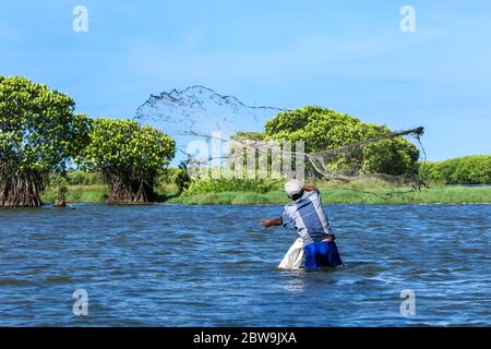 Ein srilankischer Fischer, der in hüfttiefem Wasser watet, wirft sein Netz in die Pottuvil Lagune bei Pottuvil in Sri Lanka am späten Nachmittag. Stockfoto