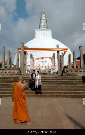 Ein buddhistischer Mönch fotografiert zwei Damen, die vor der prächtigen Ruwanwelisiya Dagoba in Anuradhapura in Zentral-Sri Lanka stehen. Stockfoto