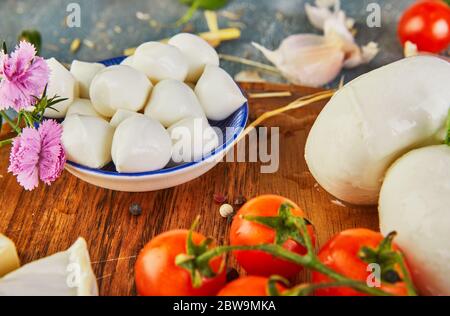 Eine Vielzahl von Käsesorten in verschiedenen Formen und Geschmacksrichtungen mit Kirschtomaten und geräucherten Oliven auf einem runden Holzteller auf blauem Hintergrund. Stockfoto