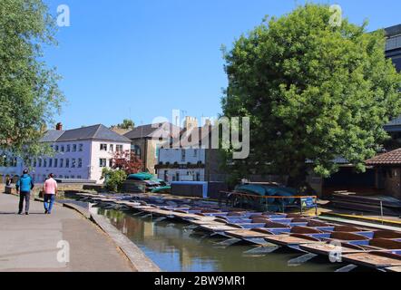 Cambridge, Großbritannien. Mai 2020. Zwei Leute gehen an Punt vorbei, die leer und untätig an einer der zahlreichen Punt-Stationen der Stadt am River Cam stehen.Cambridge, eine Stadt, die für ihre Punt-Stations berühmt ist, kann Touristen nach den aktuellen Regierungsrichtlinien nicht den Service anbieten. Scudamores, die größte Punt Hire Company der Stadt, hat den Betrieb eingestellt und die vielen Punt-Stationen der Stadt stehen aufgrund der Coronavirus-Pandemie ungenutzt. Quelle: SOPA Images Limited/Alamy Live News Stockfoto