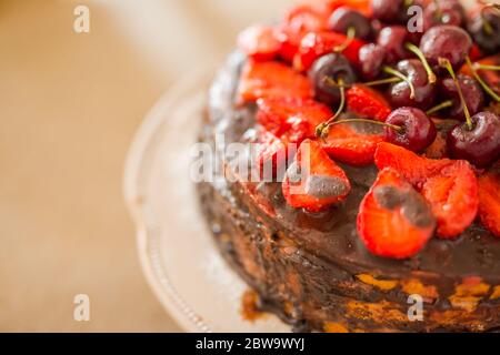 Traditionelle hausgemachte Schokoladenkuchen Süßgebäck Dessert mit brauner Glasur, Kirschen, Himbeere, Johannisbeere auf Vintage-Holz Hintergrund. Foto mit dunklen Speisen Stockfoto