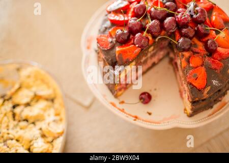 Traditionelle hausgemachte Schokoladenkuchen Süßgebäck Dessert mit brauner Glasur, Kirschen, Himbeere, Johannisbeere auf Vintage-Holz Hintergrund. Foto mit dunklen Speisen Stockfoto