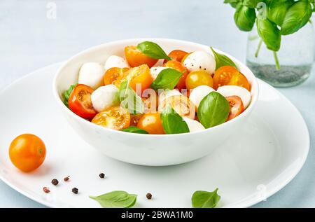 Caprese Salat mit gelben und roten Tomatenkirsche und Baby Mozzarella Käse in weißer Schüssel auf weißem Teller. Bocconcini Mozzarella Käse mit Basilikum Stockfoto