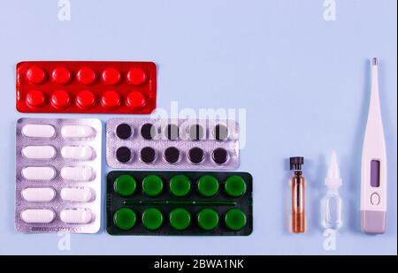 Weiße grüne schwarze und rote Pillen in Blisterpackungen. Glaskolbe und Kunststoffbirne, elektronisches Thermometer auf blauem Hintergrund. Foto von oben. Stockfoto