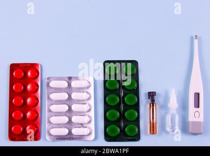 Weiße grüne schwarze und rote Pillen in Blisterpackungen. Glaskolbe und Kunststoffbirne, elektronisches Thermometer auf blauem Hintergrund. Foto von oben. Stockfoto