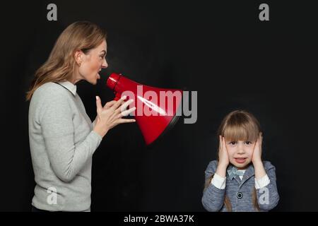 Mutter schreit im Lautsprecher zu unglücklicher Tochter. Trauriges Mädchen bedeckt ihre Ohren mit ihren Händen. Familienprobleme Konzept Stockfoto