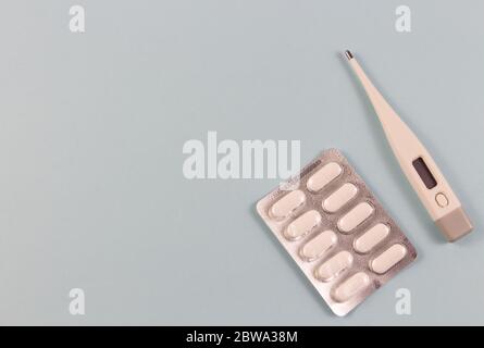 Weiße Tabletten in Blisterpackungen und elektronisches Thermometer auf blauem Hintergrund. Foto von oben. Objekte befinden sich auf Side.Copyspace für te Stockfoto
