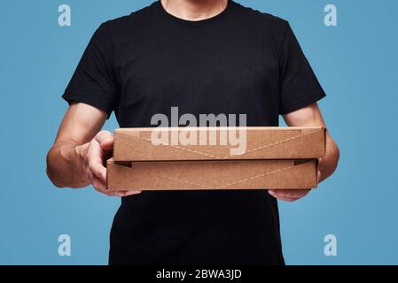 Konzept für die Lieferung von Lebensmitteln. Kurier in schwarzen Uniform-Halteboxen mit Pizza auf blauem Hintergrund Stockfoto