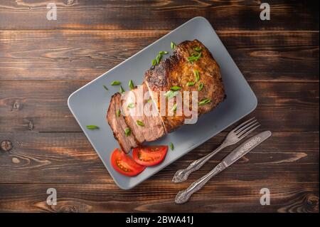 Hausgemachtes, gebackenes Schweinefleisch mit Gemüse und Gewürzen auf einem Servierbrett auf einem Holztisch. Draufsicht. Kopierbereich. Rustikaler Stil Stockfoto