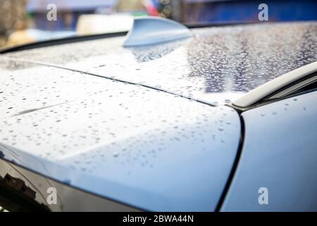 Dach eines blauen Autos mit einer Flossenantenne eines Radioempfängers, der nach Regen mit Regentropfen bedeckt ist. Nahaufnahme, Weichzeichnung. Hintergrund verwischen Stockfoto