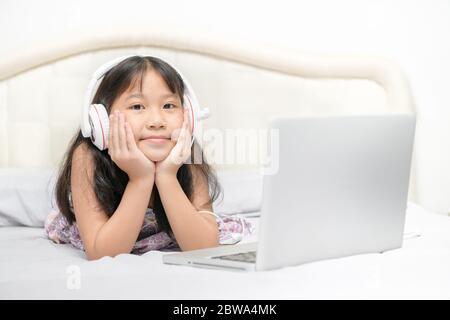 Asiatische nettes kleines Mädchen tragen Kopfhörer, um online mit einem Laptop im Schlafzimmer zu lernen. Ist ein Homeschool und Coronavirus Prevention (COVID-19). Konzept e Stockfoto