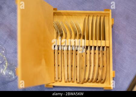 Offene Holzkiste mit Besteck 6 Messer und sechs Gabeln auf einer blauen Tischdecke. Draufsicht, Nahaufnahme, weiche Fokussierung. Stockfoto