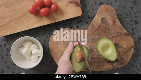 Draufsicht Mann Hände in Hälften geschnitten und öffnen reif Avocado auf Betonplatte Stockfoto