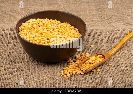 Gelbe Erbsen in einer Keramikschale auf einem Hintergrund von grobstrukturiertem Burlap. Traditionelles Getreide für die Herstellung von Suppen und Porridge. Nahaufnahme Stockfoto