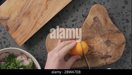 Draufsicht Mann Hände schneiden orange Zitrone auf Beton Arbeitsplatte Stockfoto