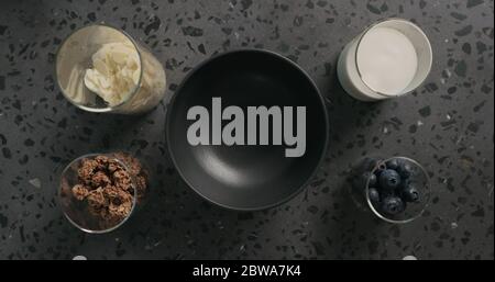 Frühstück mit Schokoladengranola, Mandelflocken und Heidelbeere in schwarzer Schüssel auf Terrazzo-Oberfläche Stockfoto