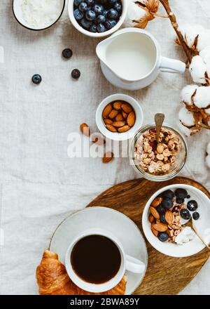 Frühstückstisch mit Müsli, Mandel, Heidelbeere, Kokosflocken, Milch, Kaffee und Croissant. Stockfoto