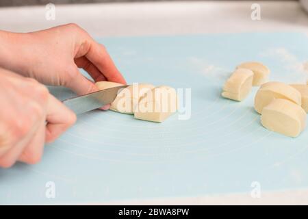 Weibliche Hand halten Messer und Schneiden kleine Stücke aus Teigrolle auf blauen Silikon-Matte Blatt, hausgemachtes Gebäck Stockfoto