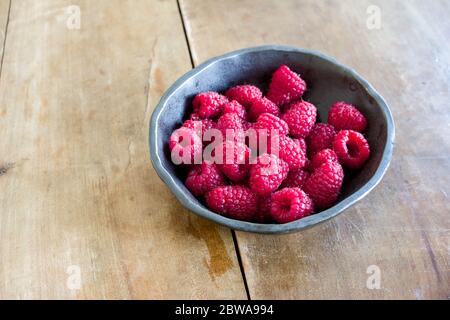 Frische saftige Himbeeren in handgefertigter schwarzer Keramikschale auf Holzbrett Stockfoto